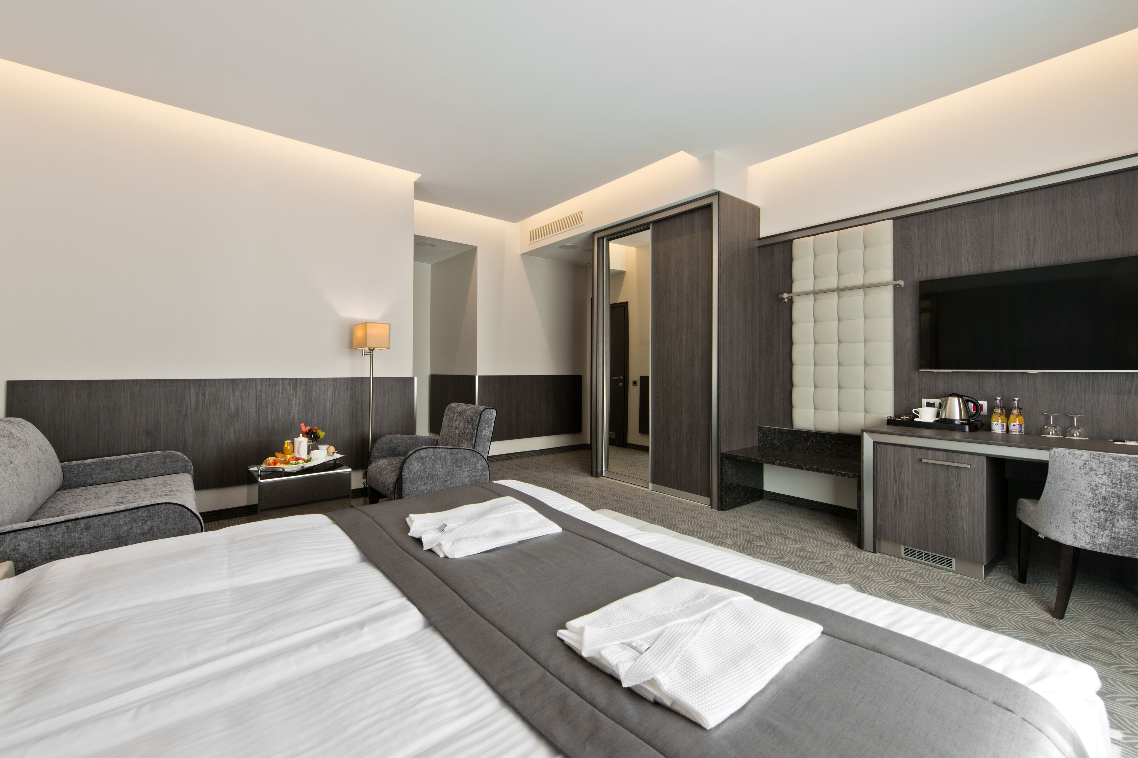 Ett modernt hotellrum med två sängar, ett skrivbord, en stol, en soffa, en TV och en minibar.