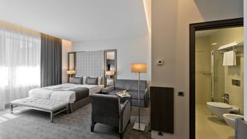 Een moderne hotelkamer met een bed, een bureau, een stoel, een bank en een badkamer met douche en toilet.