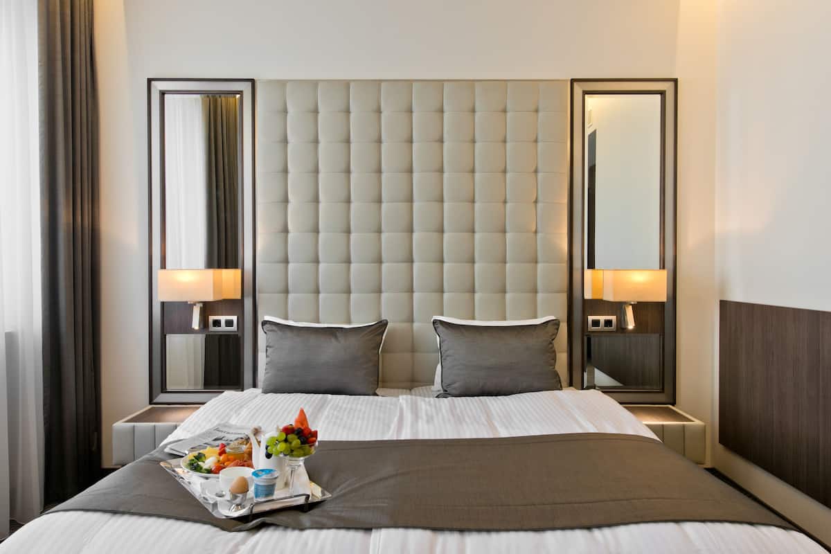 A hotel room with a large bed, two bedside tables, a headboard, and a mirror on each side.