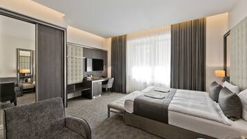 A hotel room with a bed, a desk, a chair, a TV, and a large mirror.