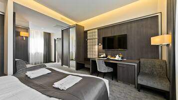 A modern hotel room with a large bed, a desk, a chair, a TV, and a bathroom visible through an open door.