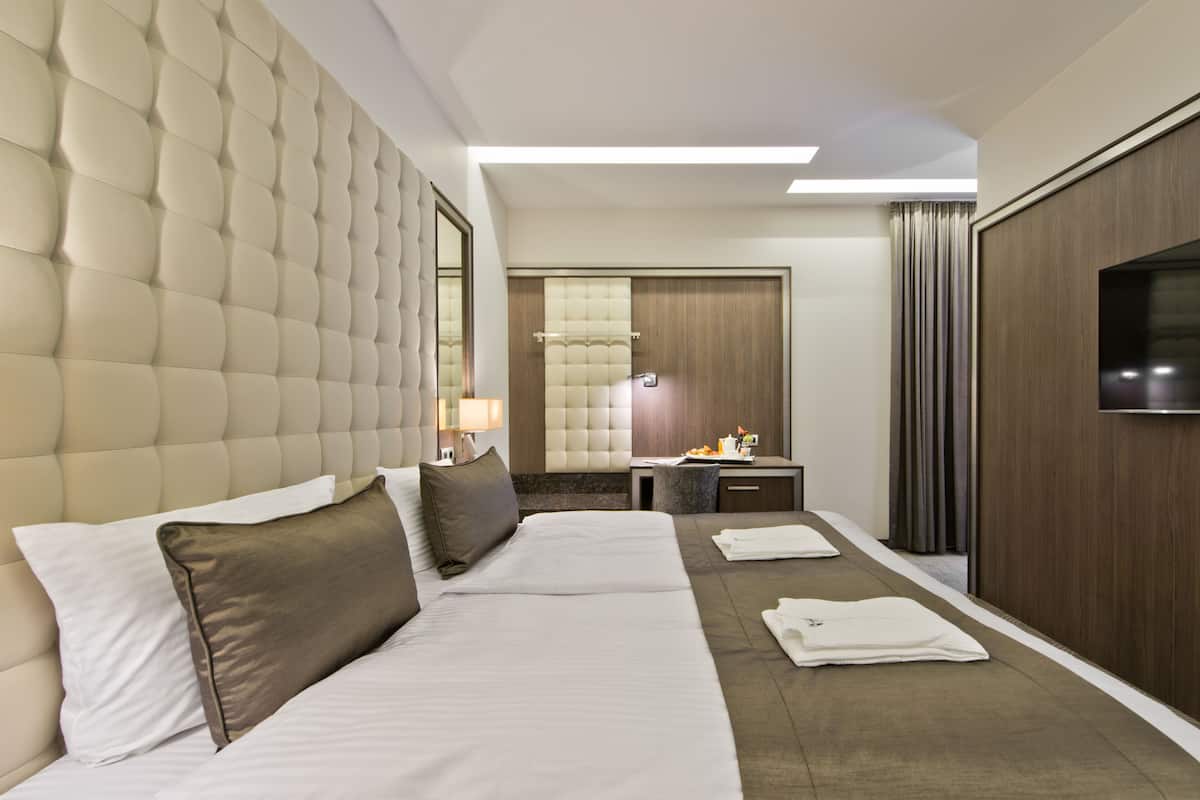 A hotel room with a large bed, a desk, a television, and a bathroom with a mirror and towel rack.