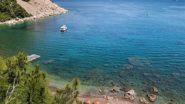 A coastal area with clear waters, rocky shore, and beach umbrellas.