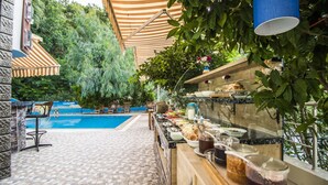 An outdoor pool area with a stone-tiled floor, a pool, and a bar area with a variety of food and drink options.