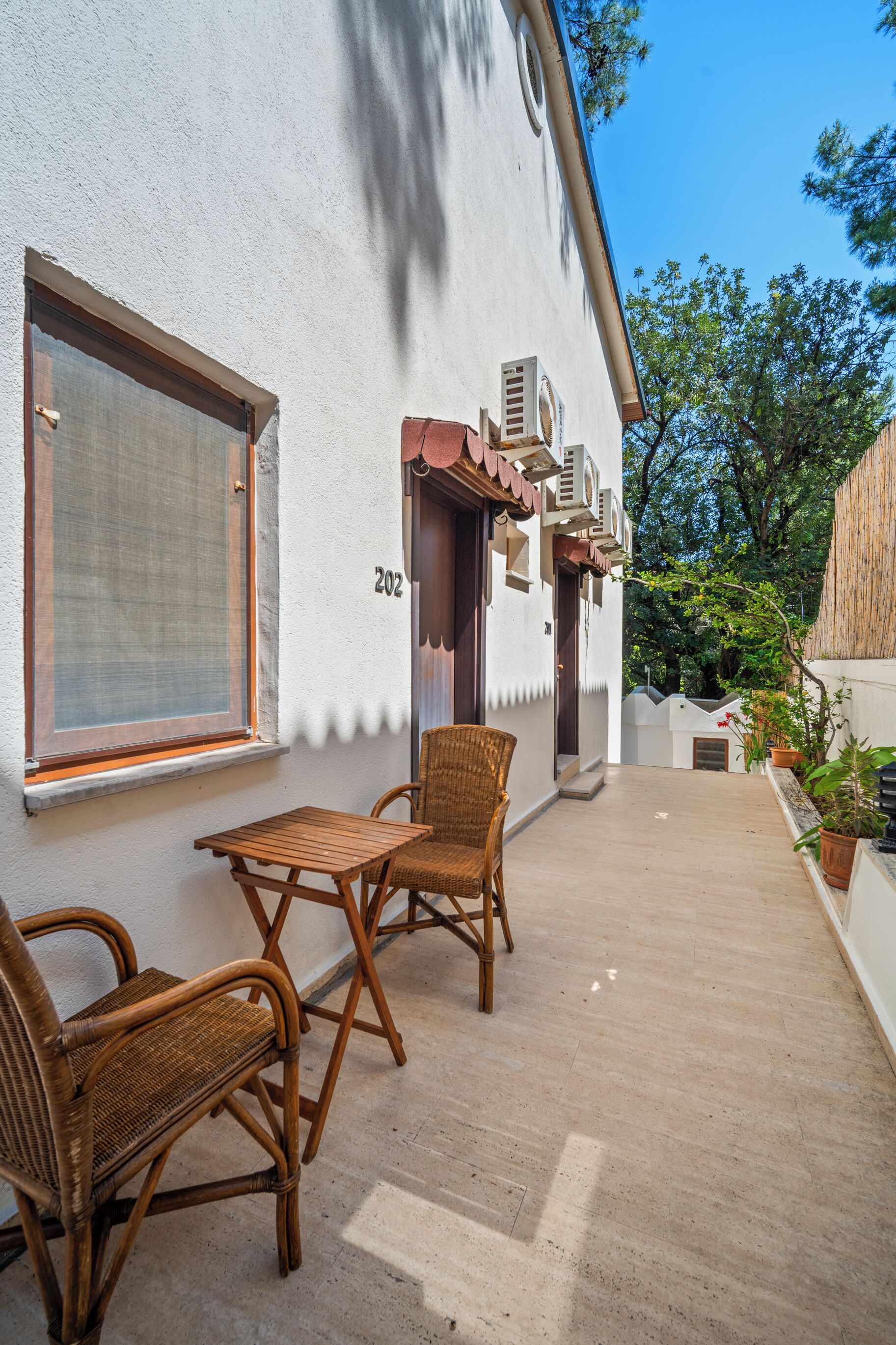 A room with a large window, a door, and a small table with two wicker chairs.