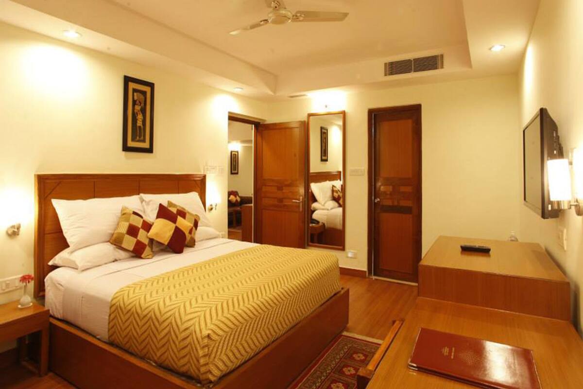 A hotel room with a bed, bedside tables, a desk, a chair, a mirror, a ceiling fan, and a TV.