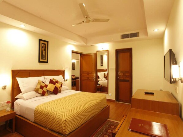 Habitación de hotel con cama, mesitas de noche, escritorio, silla, espejo, ventilador de techo y televisor.