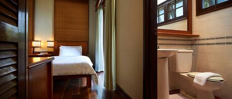 A hotel room with a bed, bedside table, lamp, window, and a bathroom with a toilet and sink.
