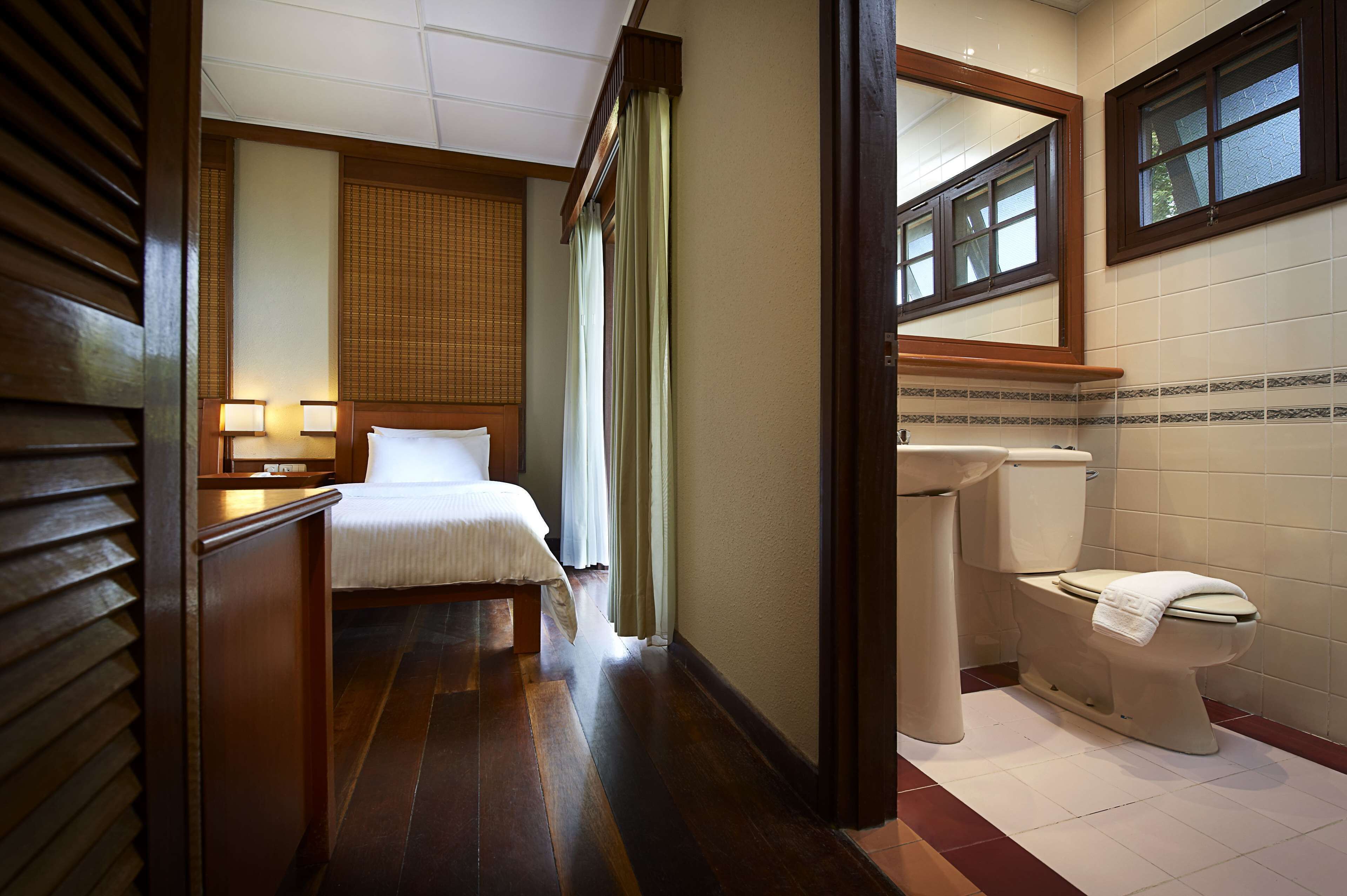 A hotel room with a bed, bedside lamps, a bathroom with a toilet, sink, and mirror.