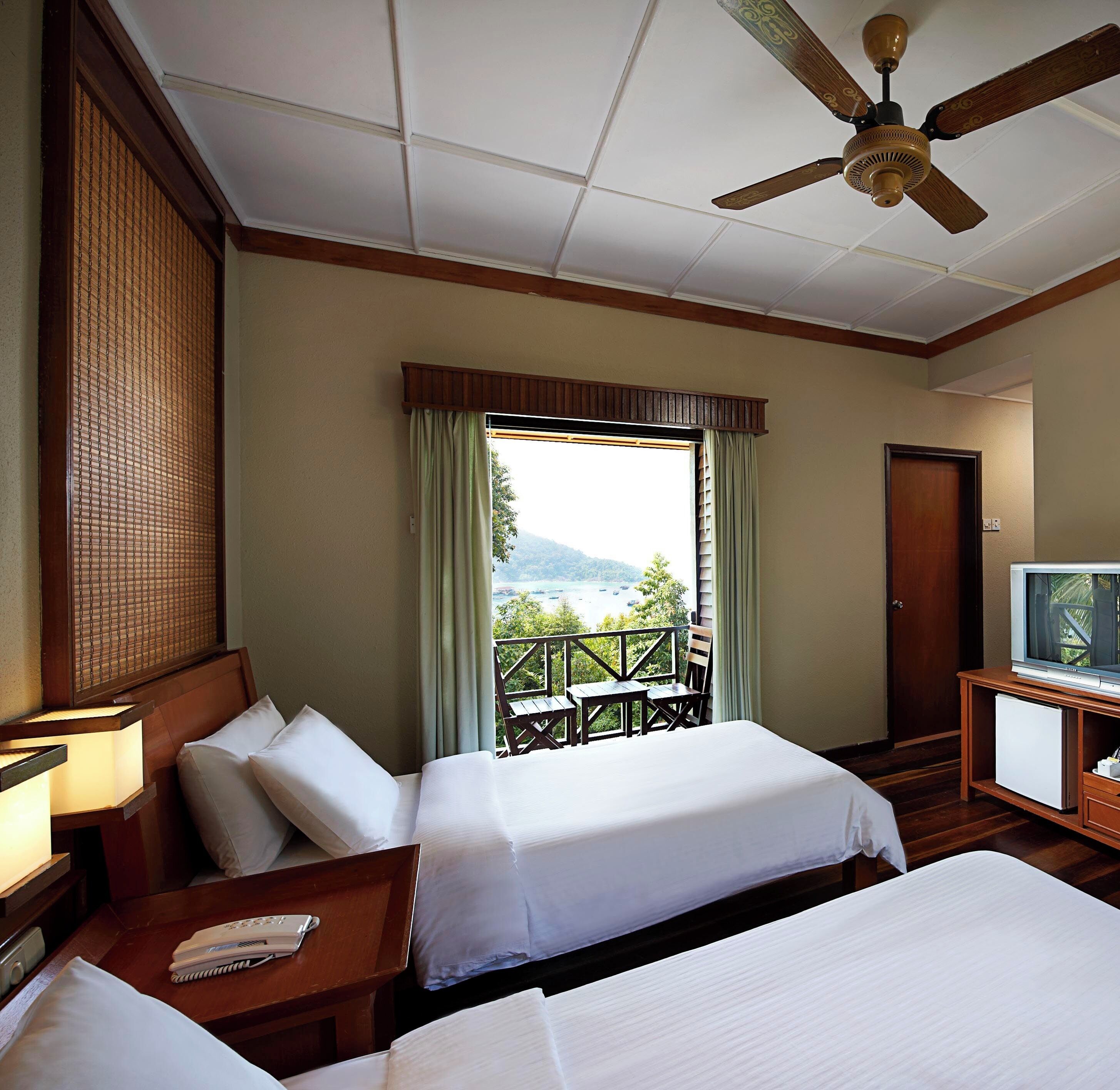 A hotel room with two beds, a TV, a desk with a phone, and a balcony with a view of the mountains.