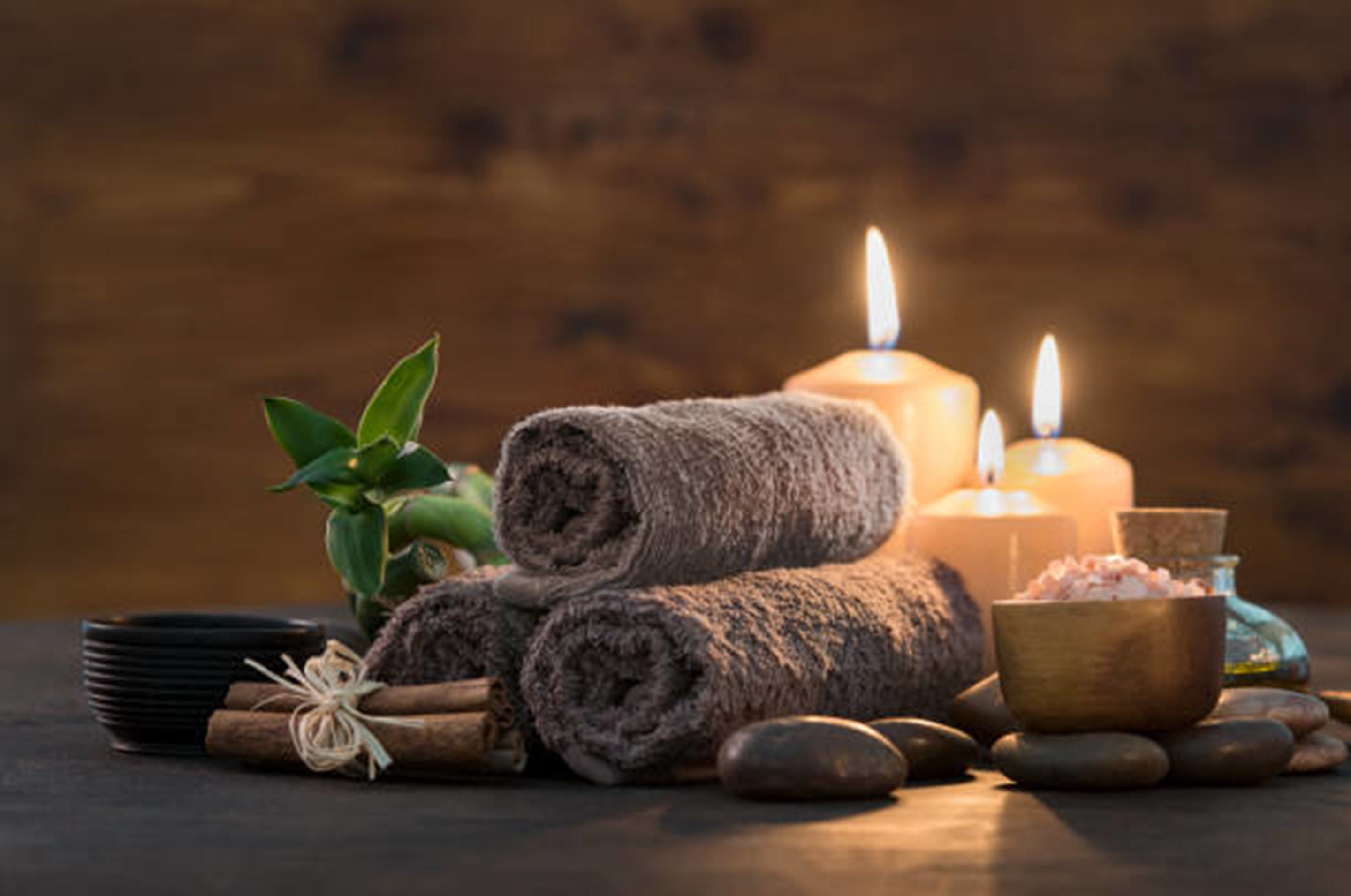 A spa setting with candles, rolled towels, a bowl of bath salts, and a small plant.