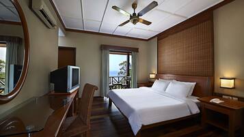 Quarto de hotel com cama, televisão, escrivaninha, cadeira, varanda com vista e ventoinha no teto.