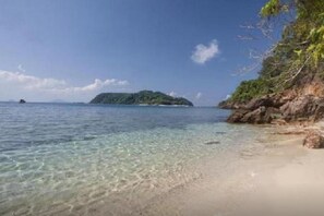 A beach with clear shallow waters, a rocky shoreline, and a distant island. - Redang Island Resort (Redang Island)