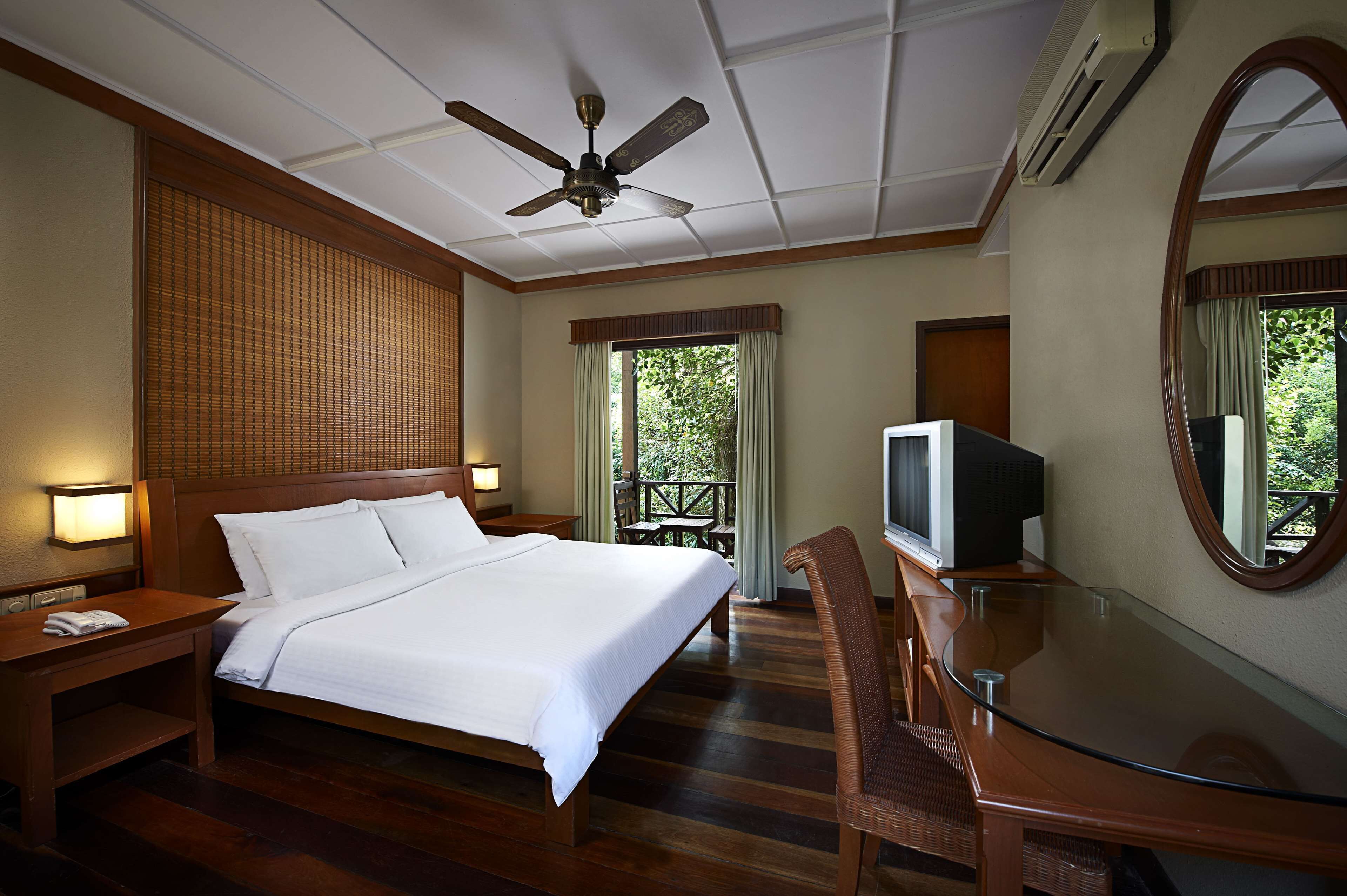 Habitación de hotel con una cama grande, un televisor, una mesita de vidrio y un ventilador de techo.