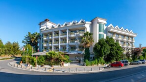 Un hotel de varios pisos con balcones, una entrada principal y un estacionamiento.