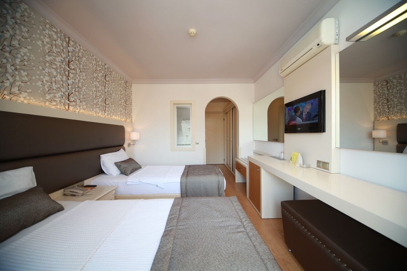 A hotel room with two beds, a desk, a TV, and a decorative wall.