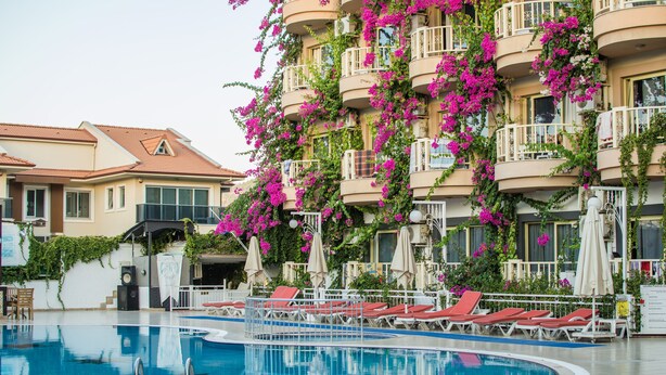 Una piscina con sillas reclinables rojas y un edificio con balcones cubiertos de flores rosadas.