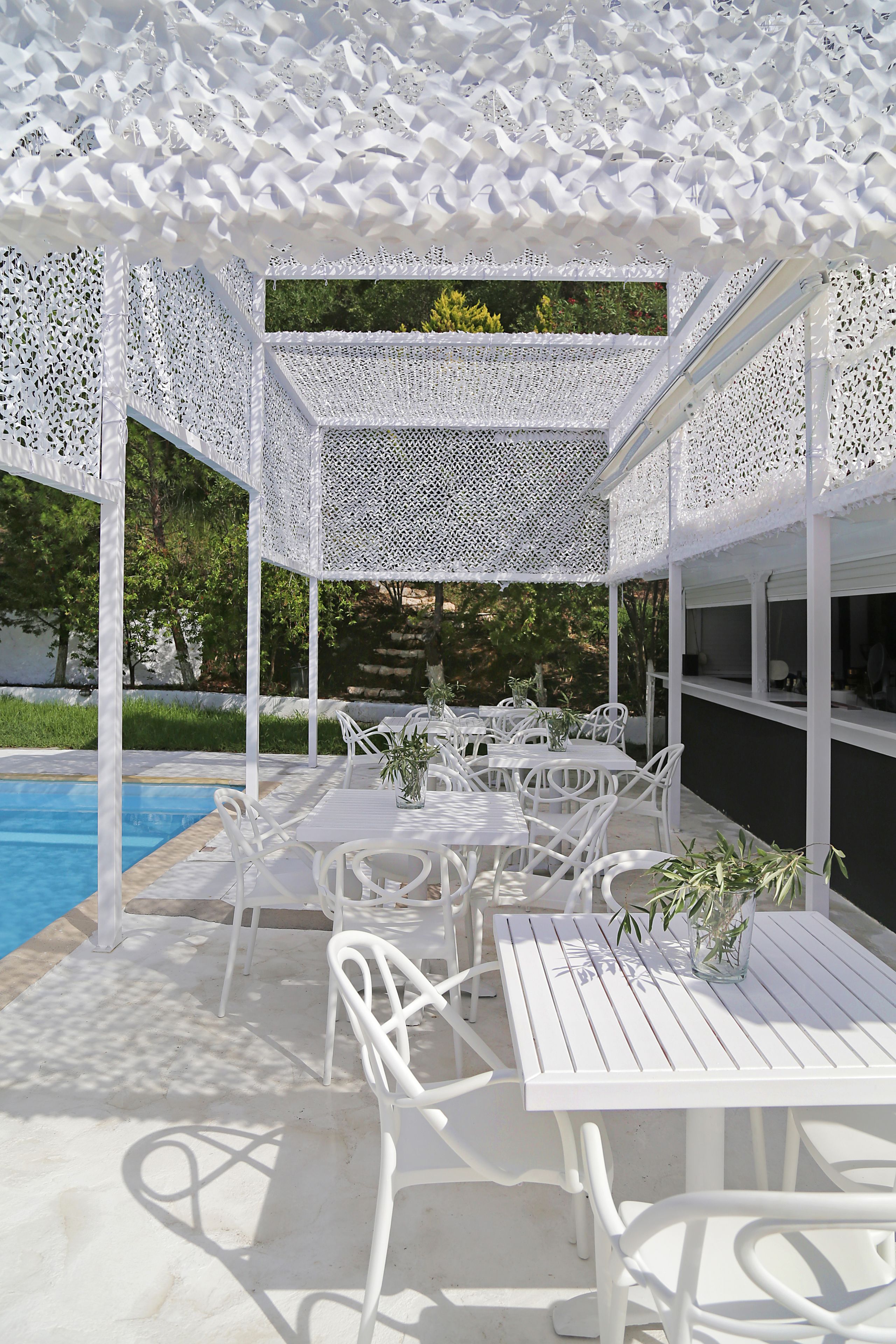 Ein überdachter Außenbereich mit weißen Möbeln und einem Pool im Hintergrund.