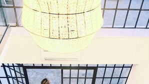 Un hall d’entrée spacieux, doté d’un plafond haut, d’un grand lustre et offrant une vue à travers une fenêtre à motifs géométriques.