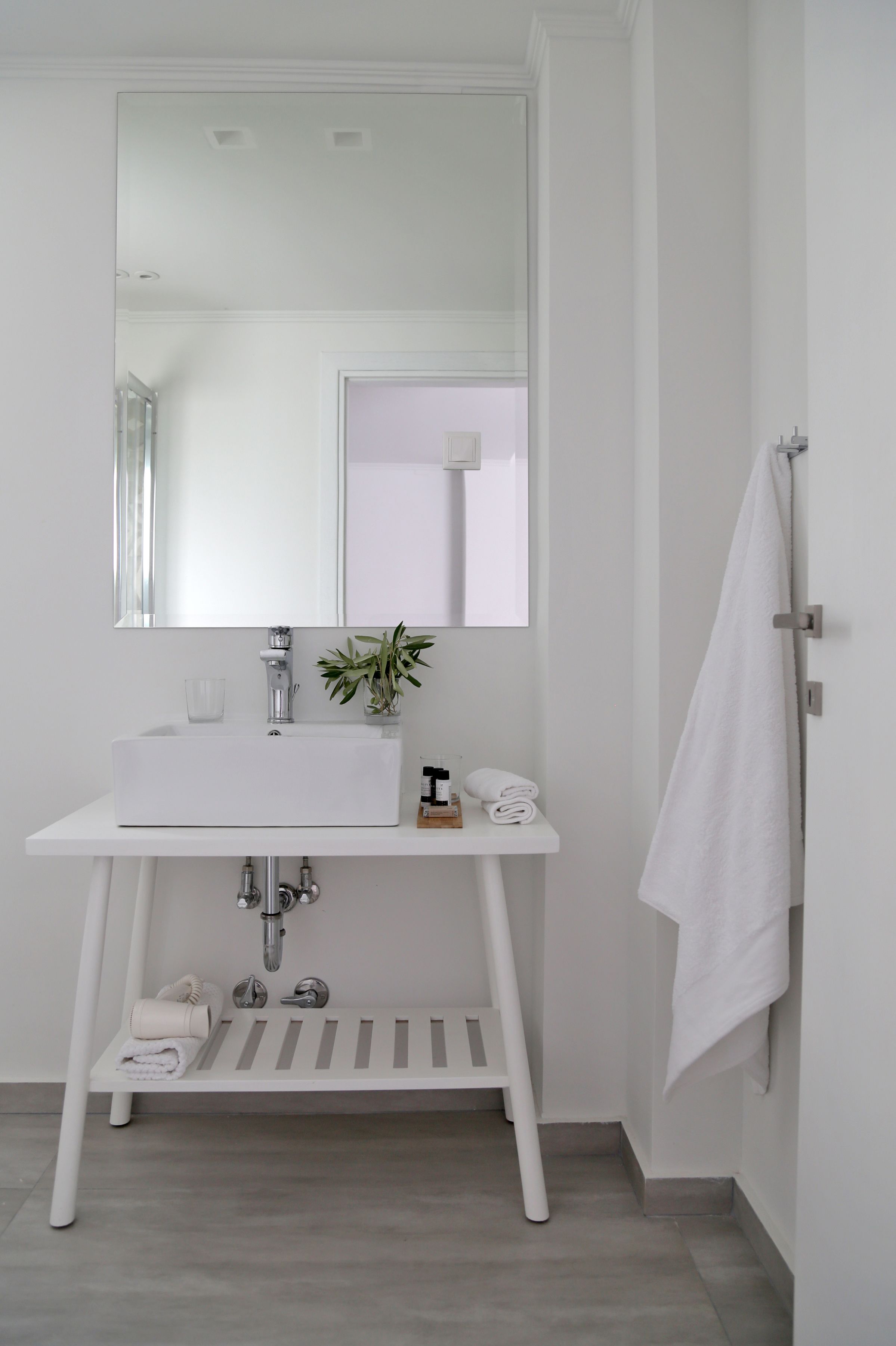 A white bathroom with a rectangular sink, a mirror above it, a towel rack, and a small potted plant on the sink.