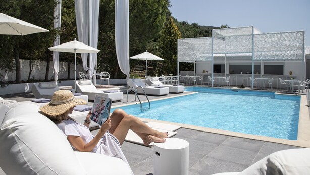 Un espace aménagé au bord de la piscine, avec des chaises longues, des parasols et une personne qui lit un magazine.