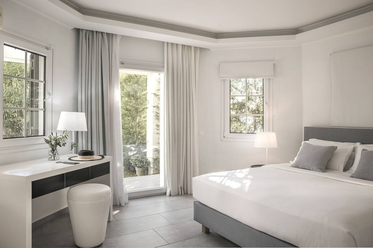 A modern hotel room with a large bed, a bedside table, a desk, and a window with curtains.