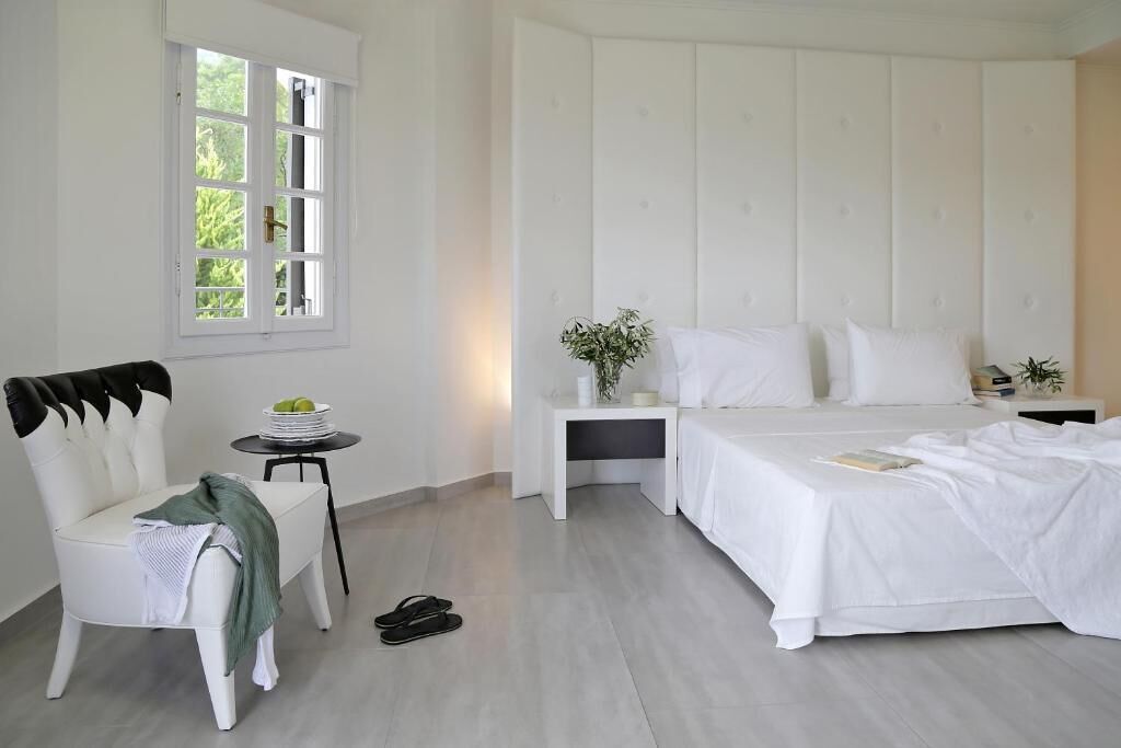 Un dormitorio con cama, una silla, una mesita, una mesita de noche y una ventana.