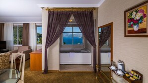 A hotel room with a view of the sea, a sofa, a glass table, a bathtub, and a mirror. - Lâ€™ETOILE BEACH HOTEL - All inclusive (Marmaris)