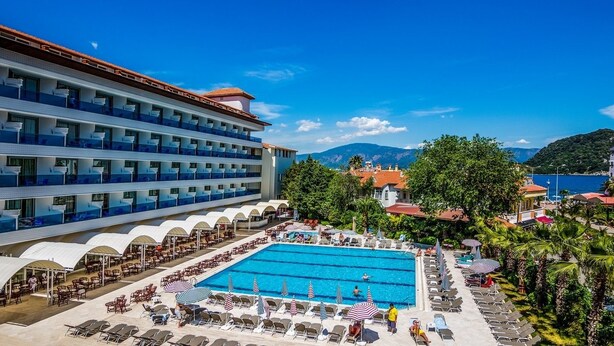 A hotel with a large swimming pool, multiple balconies, and a view of the mountains. - Lâ€™ETOILE BEACH HOTEL - All inclusive (Marmaris)