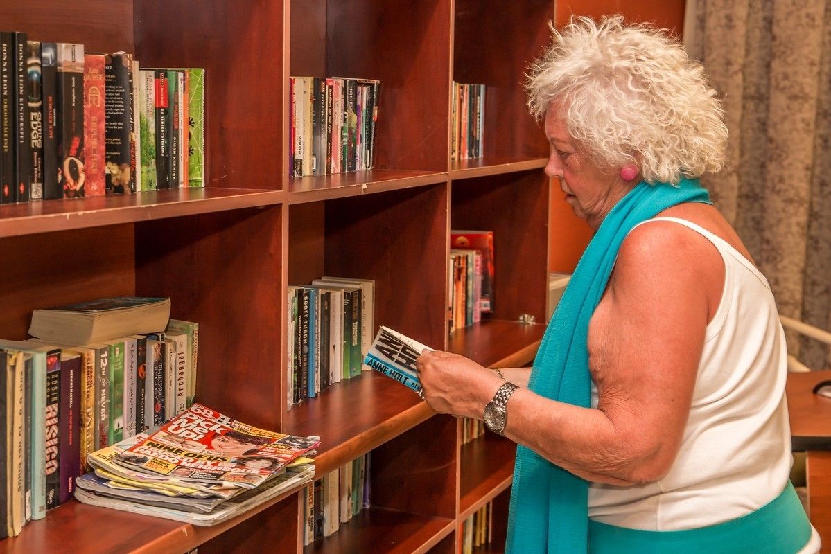 Una persona leyendo una revista en una habitación con estanterías de madera llenas de libros y revistas.