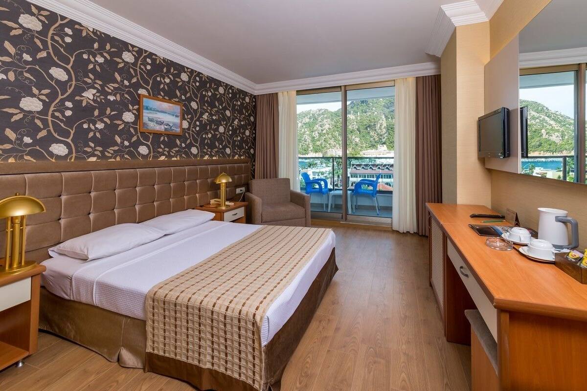 Une chambre d’hôtel comprenant un lit, un bureau, une chaise, une télévision et un balcon avec vue sur la mer.