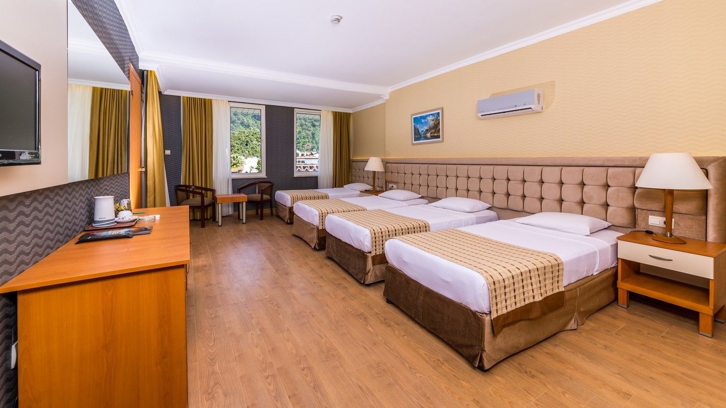 Habitación de hotel con tres camas, un escritorio, una silla, un televisor y un equipo de aire acondicionado.