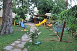 A playground with a slide, swings, and a small tree in the center.