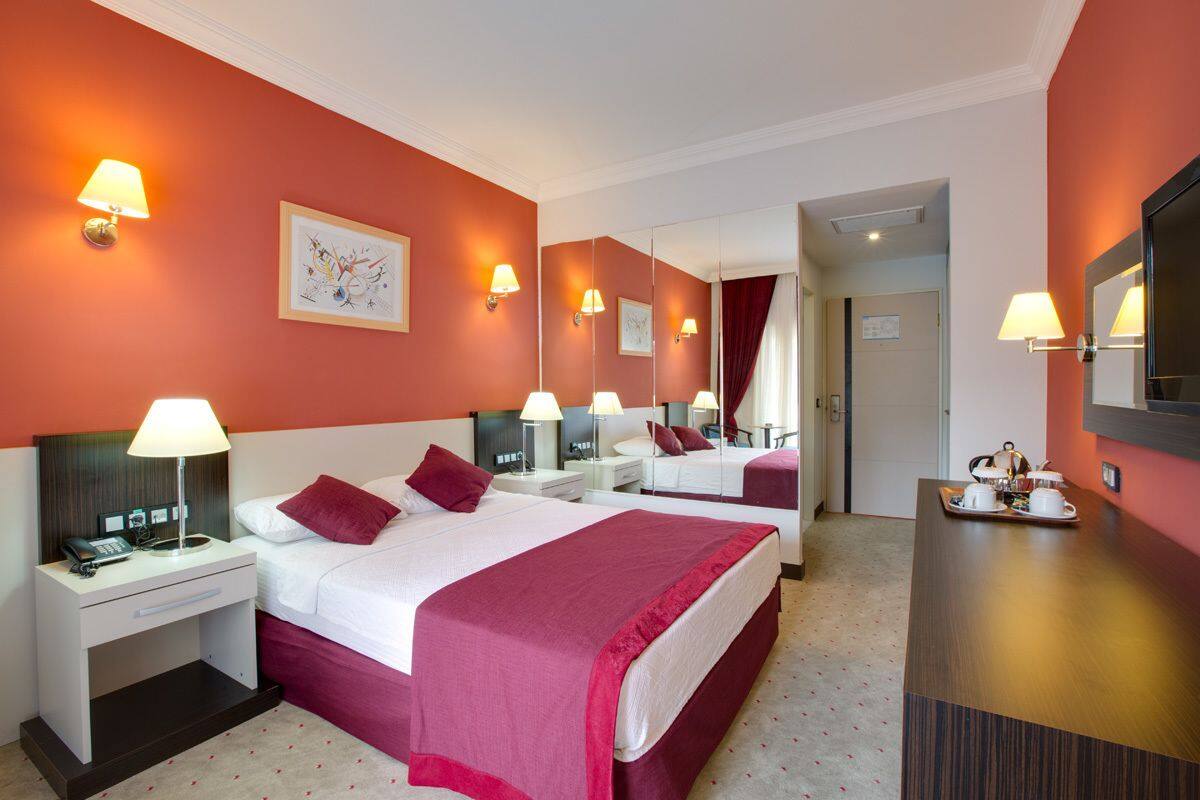 A hotel room with two beds, a desk with a lamp, a mirror, and a breakfast tray on the dresser.