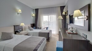 Une chambre d’hôtel avec deux lits, un bureau avec une lampe, une télévision et une fenêtre avec des rideaux.