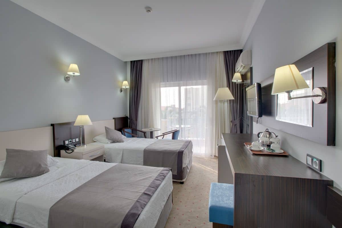A hotel room with two beds, a desk with a lamp, a TV, and a window with curtains.