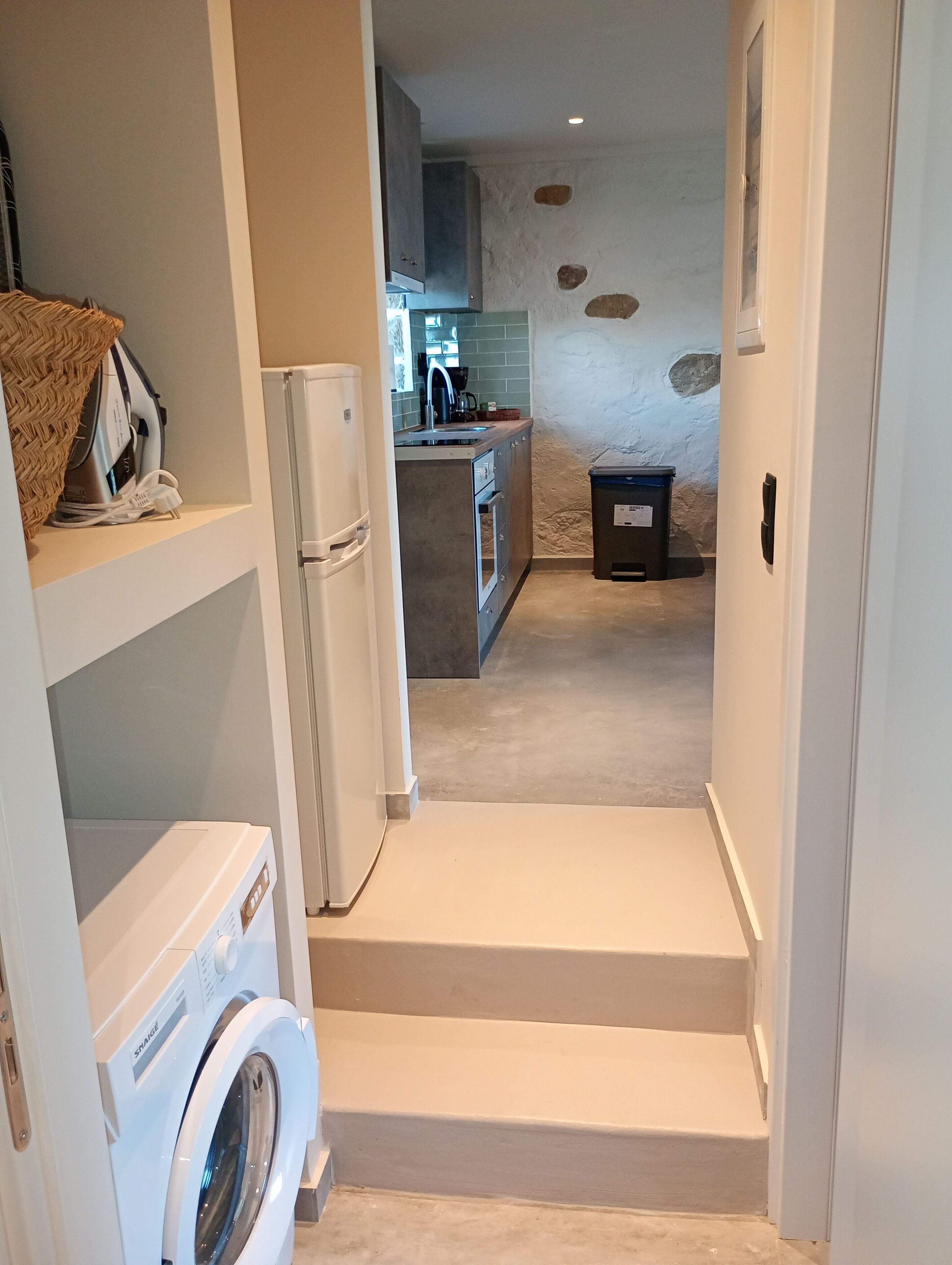 A laundry area with a washing machine and dryer, a kitchen with a sink and cabinets, and a small stool.