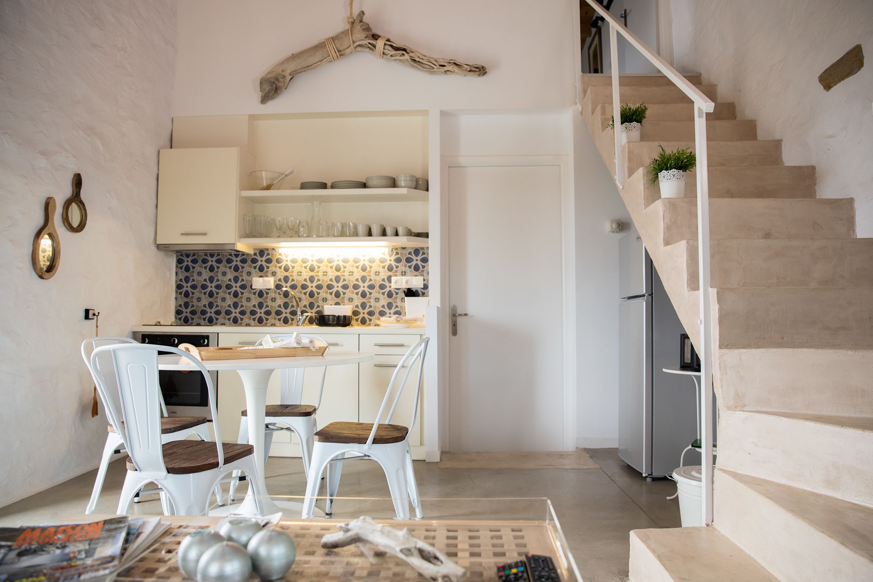 A modern kitchen with white cabinets, a patterned backsplash, and a dining area with white chairs and a wooden table.
