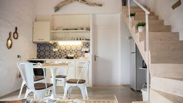 A modern kitchen with white cabinets, a patterned backsplash, and a dining area with white chairs and a wooden table.
