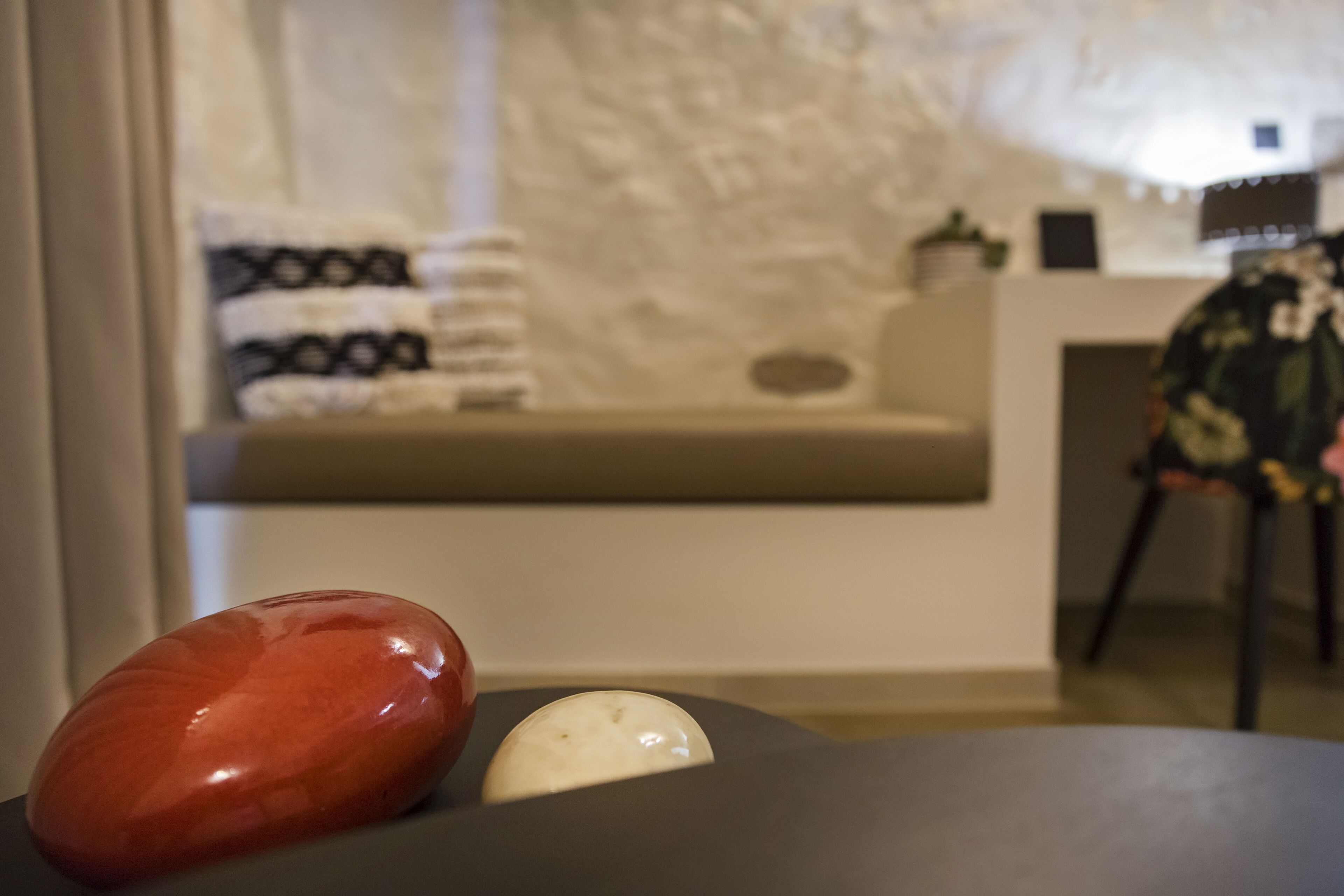 Una habitación con una mesa negra, una piedra roja y blanca, y un cojín blanco sobre un sofá beige.