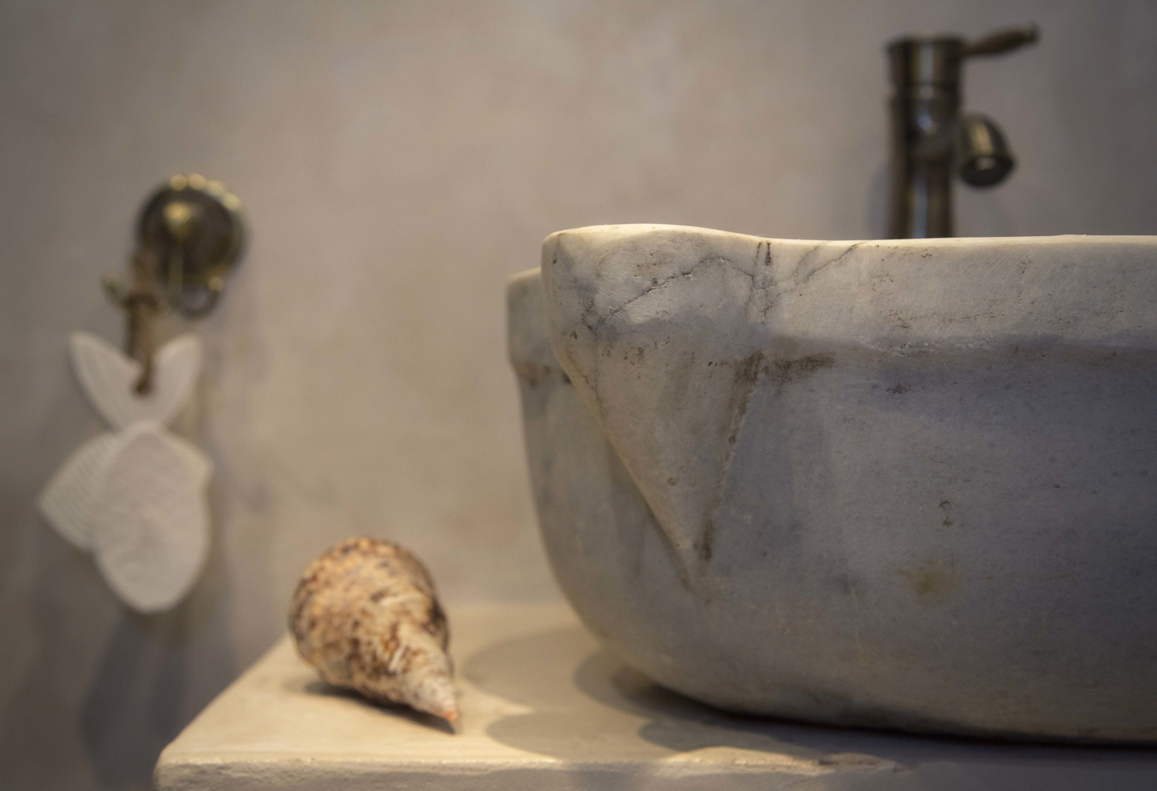 Une salle de bain avec un lavabo en marbre, un robinet et un coquillage posé sur le comptoir.