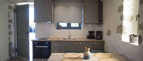 A compact kitchen with a dining area, featuring a built-in oven, a coffee machine, and a window with a view.