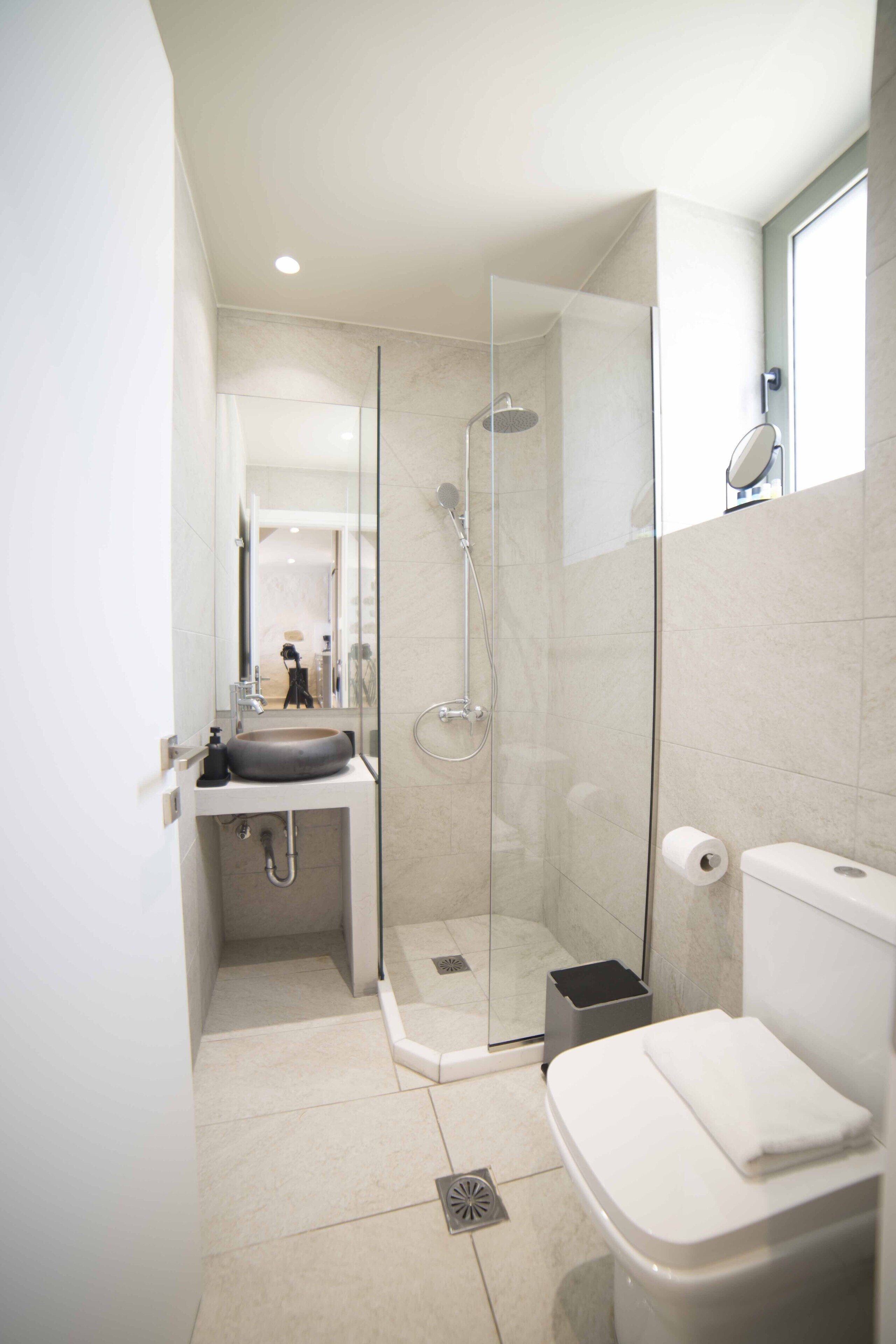 A modern bathroom with a glass-enclosed shower, a white sink, and a toilet.