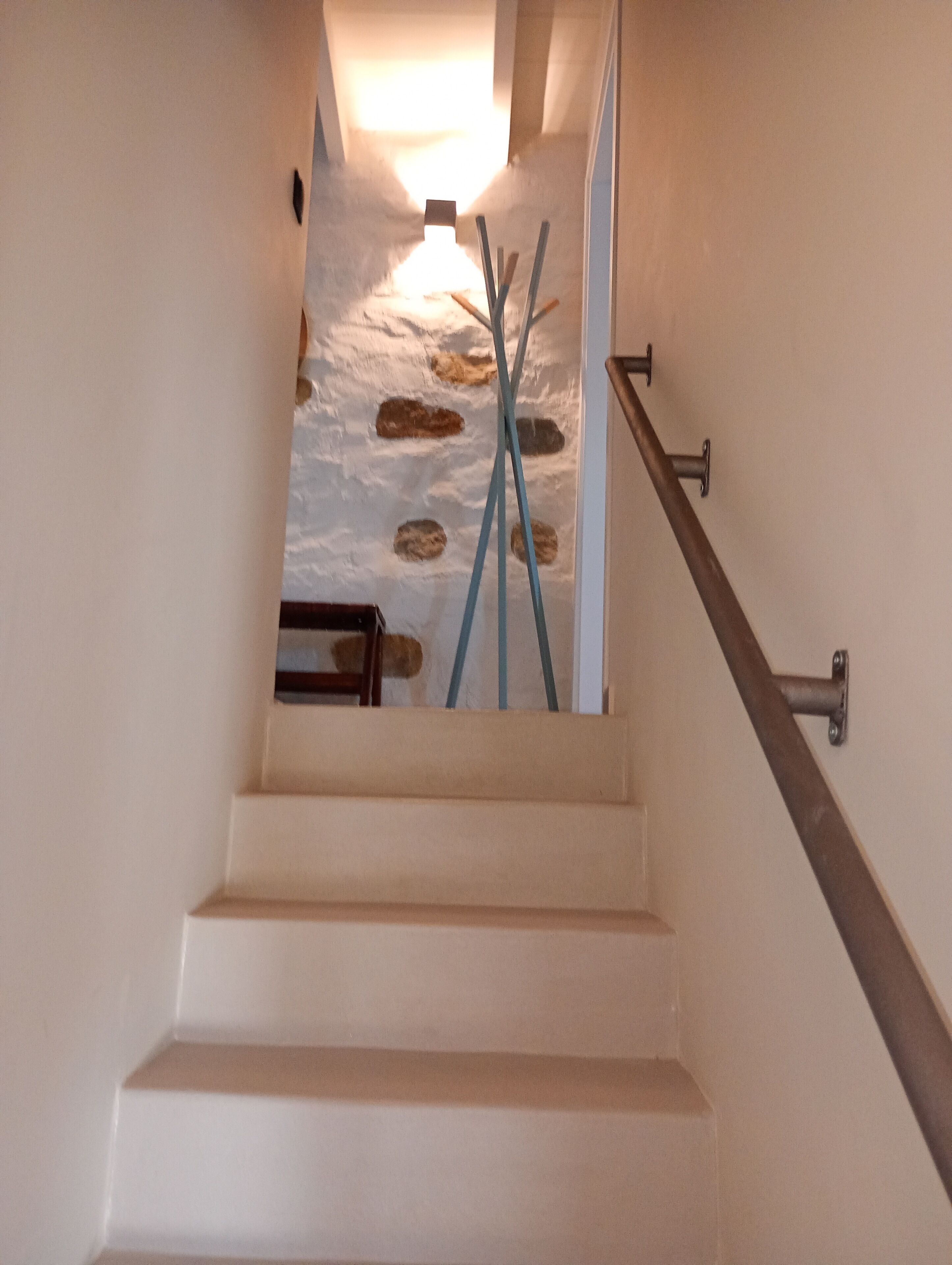 A staircase with a stone wall at the top, a wooden handrail, and a metal handrail.