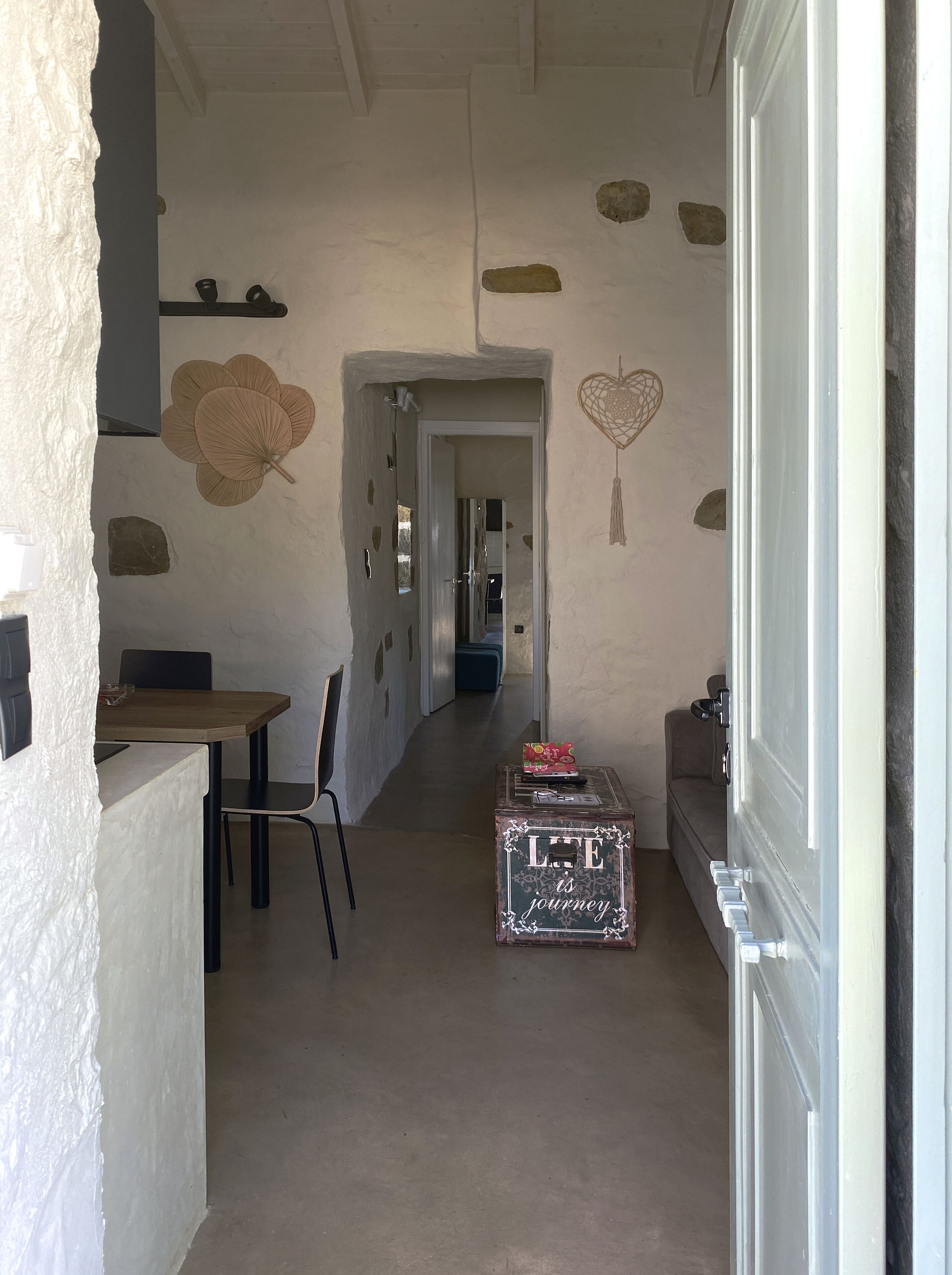 A hallway with a table and chairs, a decorative wall with stones and a heart design, and a suitcase with the text "LIFE is journey".