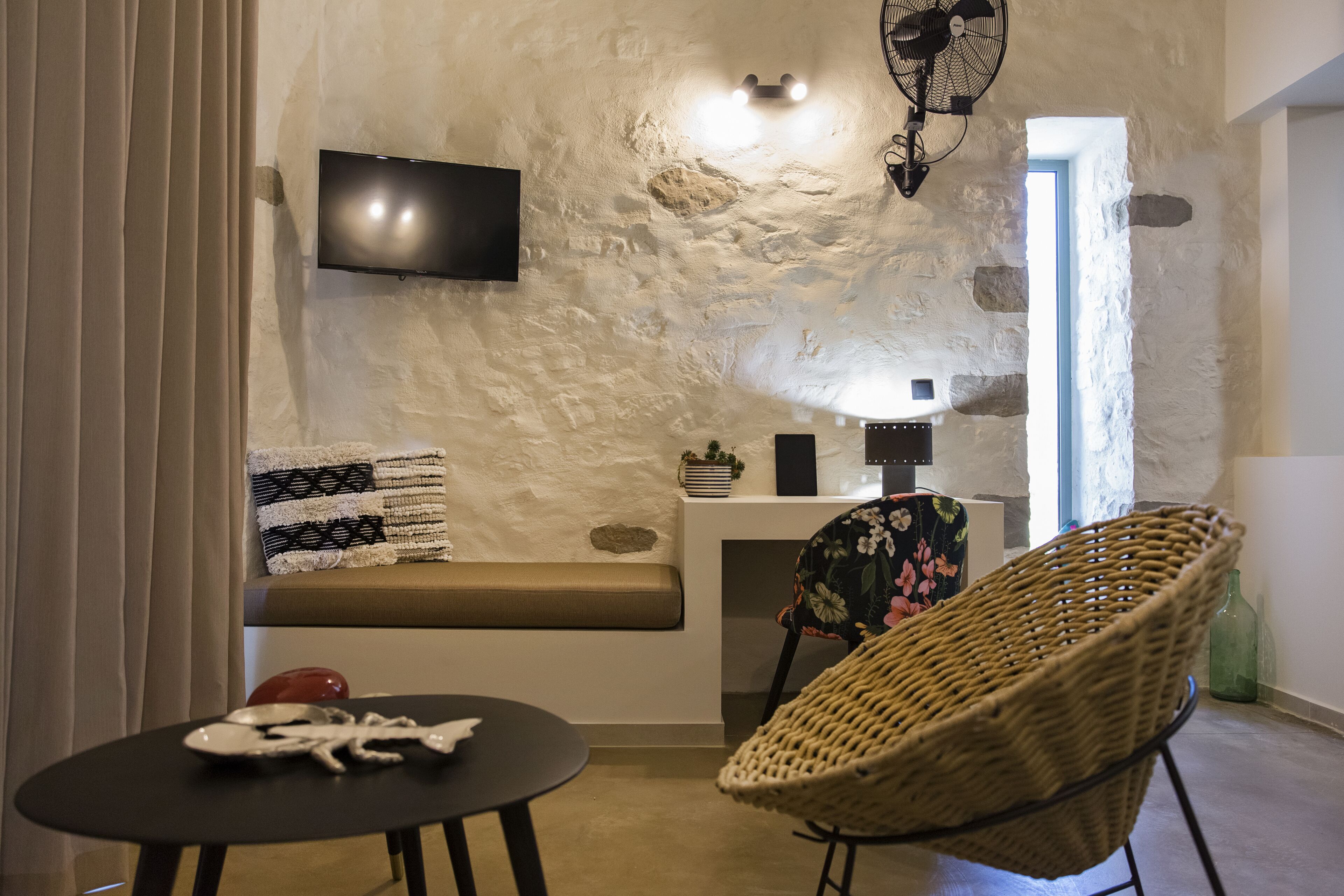 Ein gemütlicher Wohnbereich mit Steinwand, Flachbildfernseher, einem gewebten Sessel und einem kleinen Tisch mit einer Dekoration.