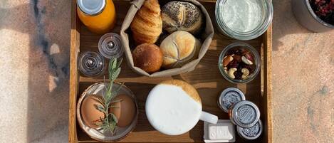 A wooden tray with croissants, a bottle of orange juice, a glass of milk, a small plant, and jars of spreads.