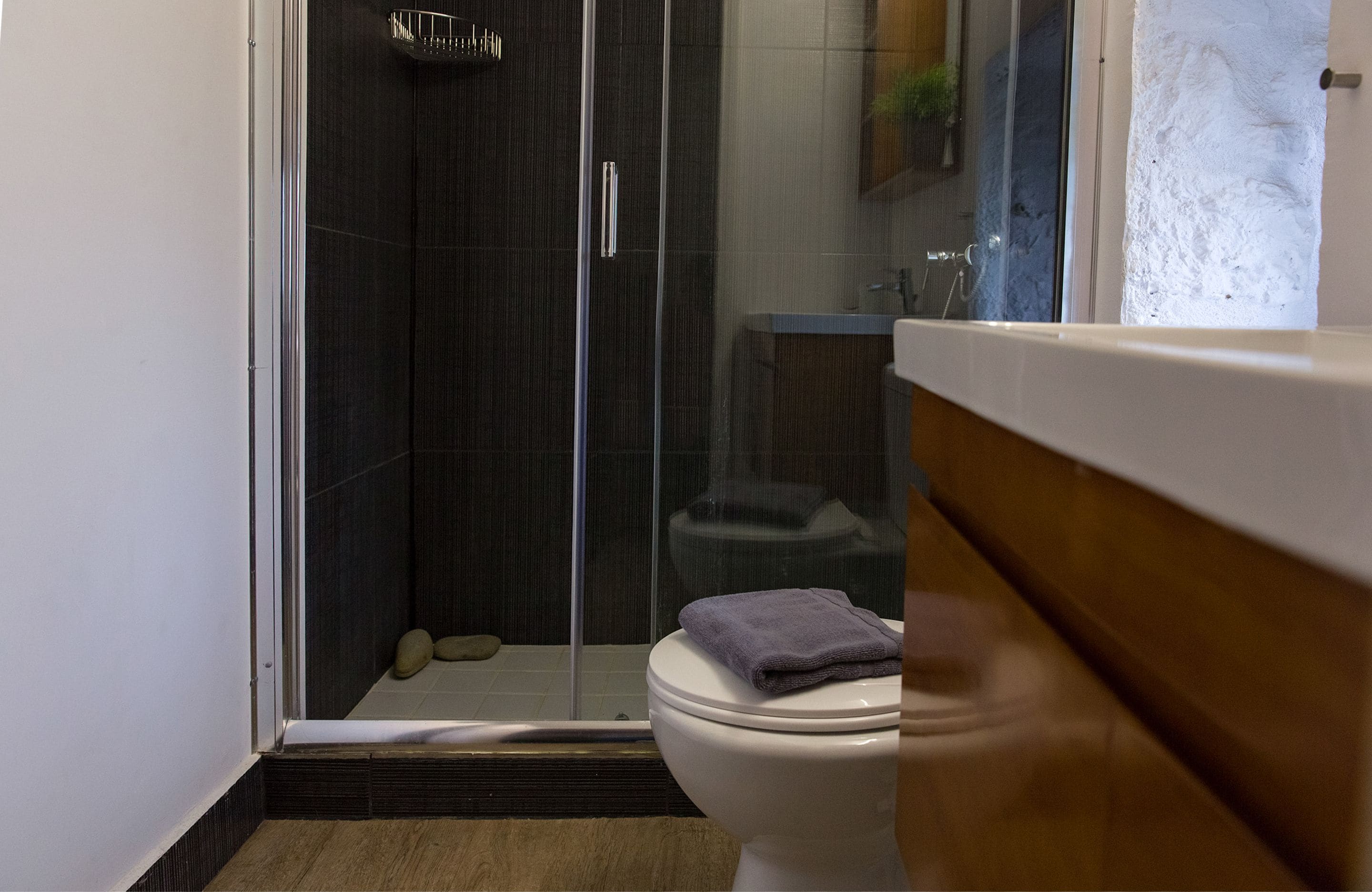 Un baño moderno con ducha de vidrio, inodoro blanco y tocador de madera.