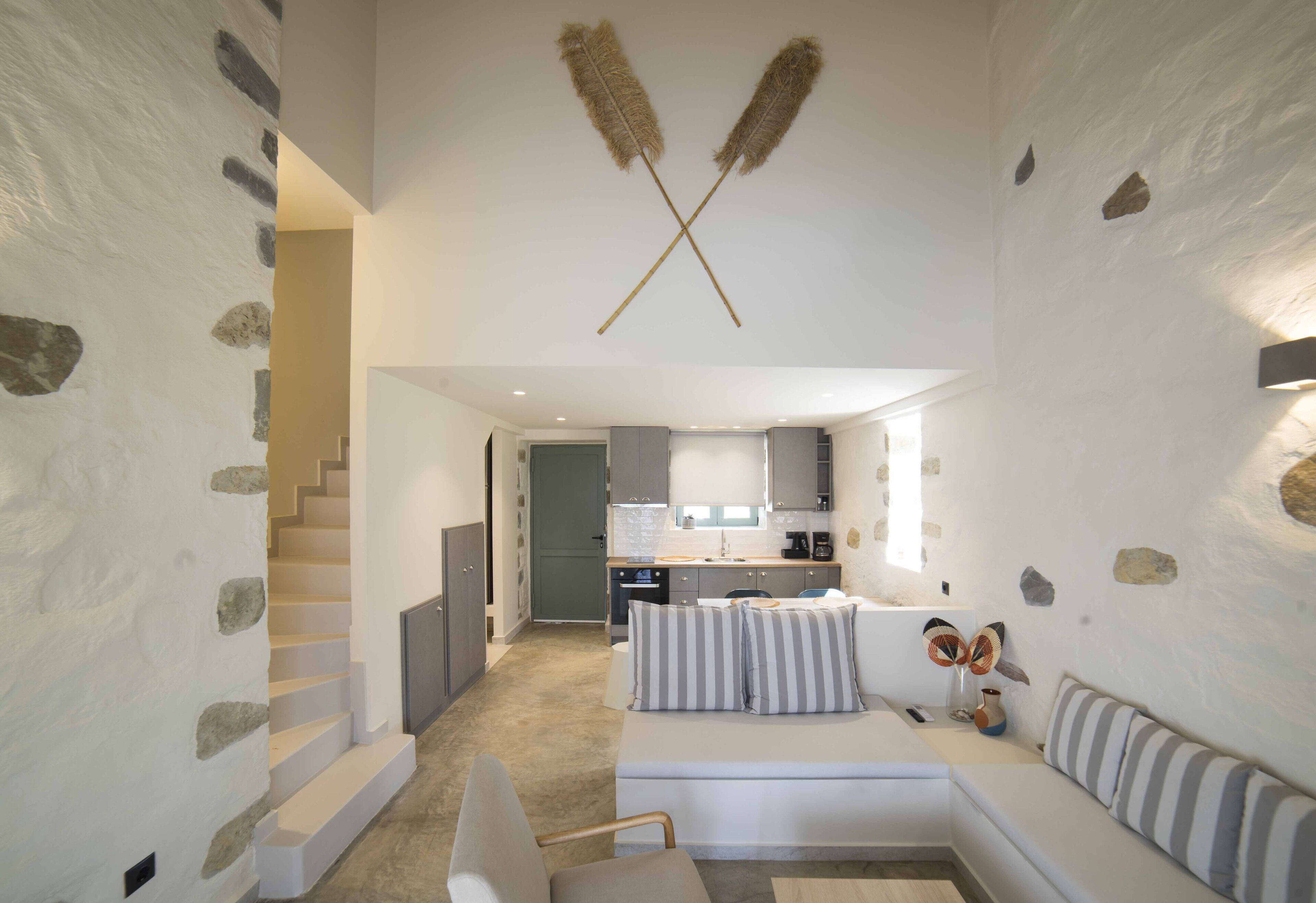Un interior moderno con una pared de piedra, una escalera, una cocina y una sala de estar con sofá y cojines.