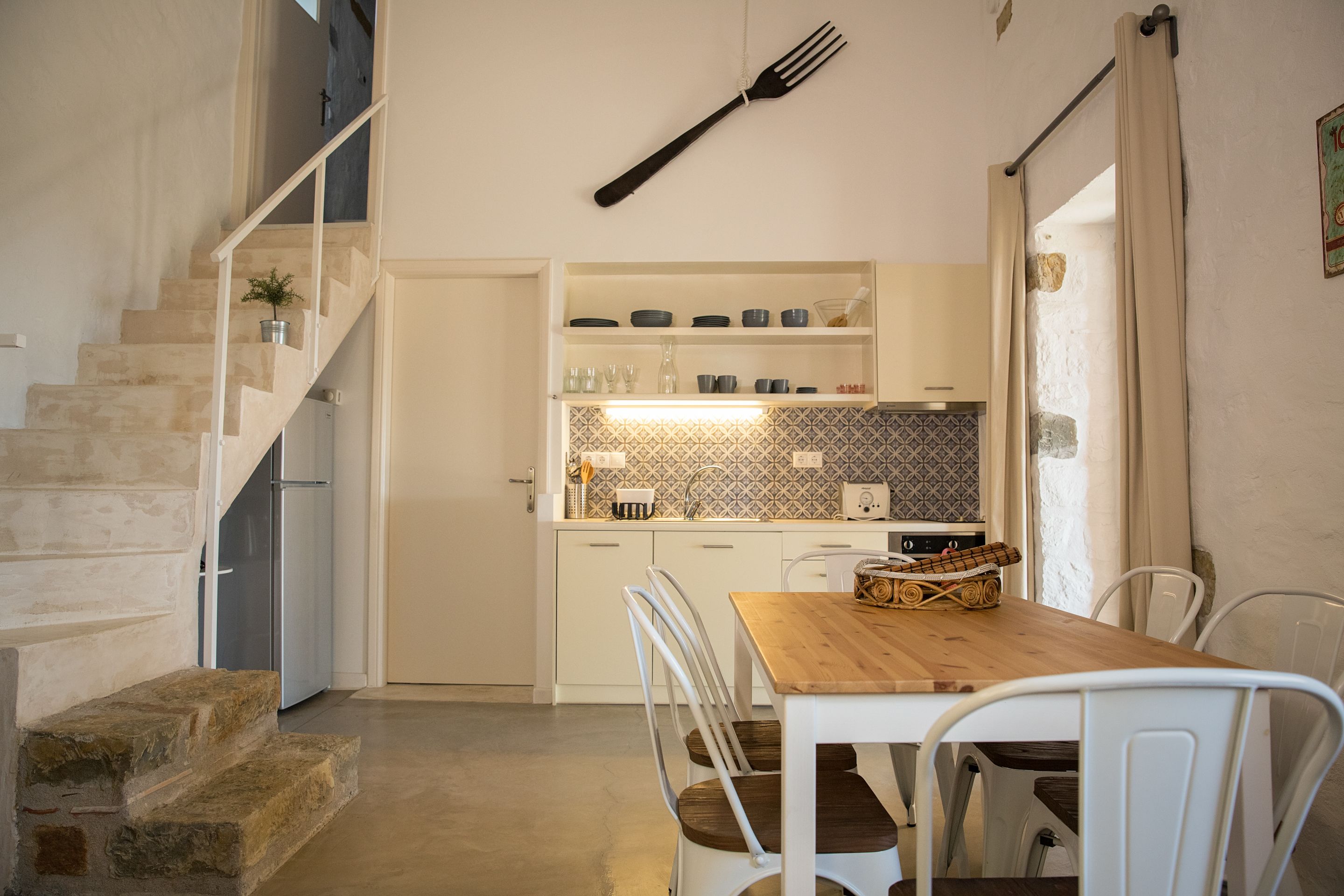 Een keuken met witte kastjes, een houten tafel en een trap.